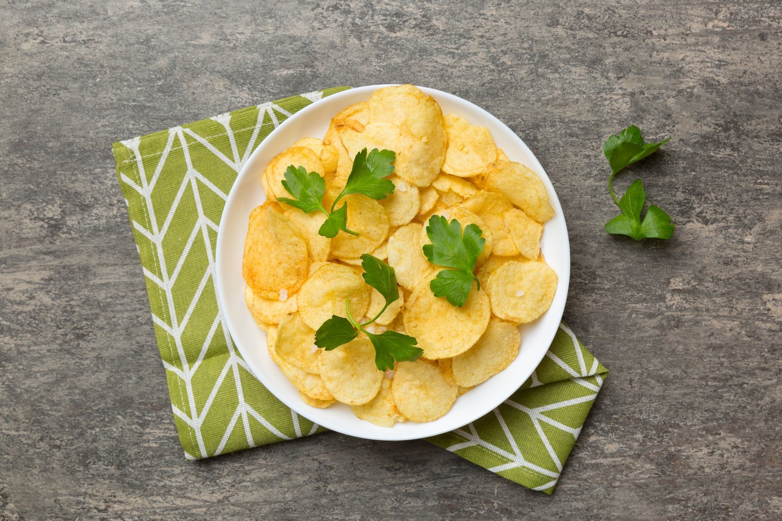 Potato chips on bowl with napkin on colored background. Delicious crispy potato chips in bowl.